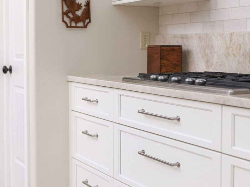Tulsa kitchen remodel featuring white cabinet and drawer storage, a gas cooktop, a vent hood, and a subway tile backsplash. The design is completed with quartz countertops.