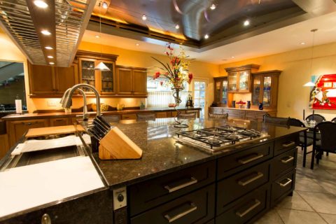 Tulsa kitchen design and remodel featuring a kitchen island with a vent hood, cabinet and drawer storage, a gas cooktop, a marble counter, and a Galley Workstation.