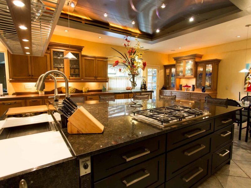 Tulsa kitchen design and remodel featuring a kitchen island with a vent hood, cabinet and drawer storage, a gas cooktop, a marble counter, and a Galley Workstation.