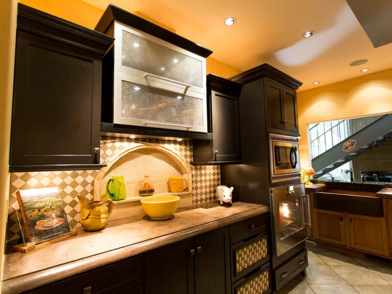 Tulsa kitchen design and remodel featuring a kitchen niche with a tile backsplash, a concrete countertop, lighted wall cabinet storage, crown molding, and double ovens.