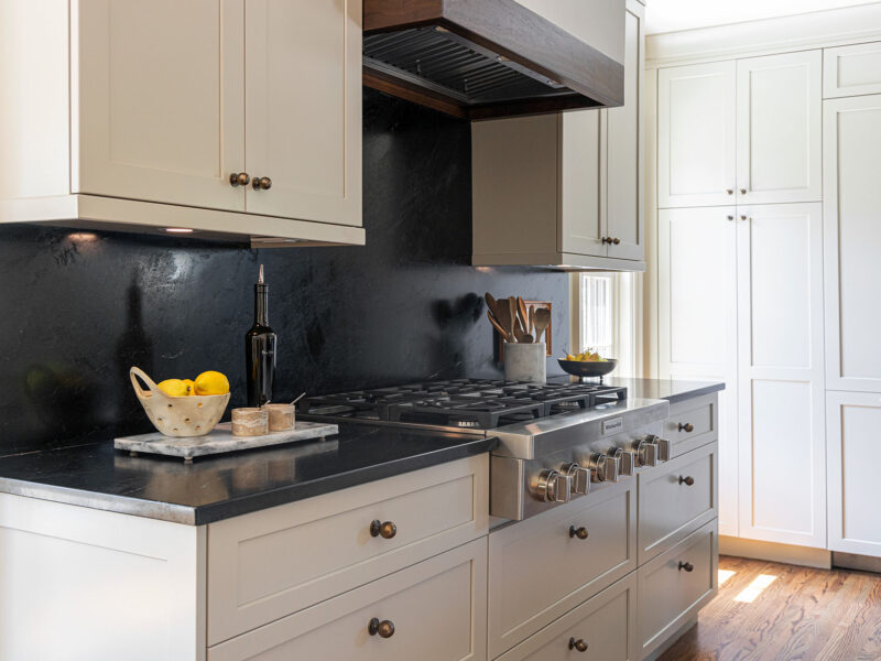 Tulsa kitchen remodel featuring a range top with a vent insert, dark countertops and backsplash, cream-colored cabinet storage, and a tall panel-front refrigerator.
