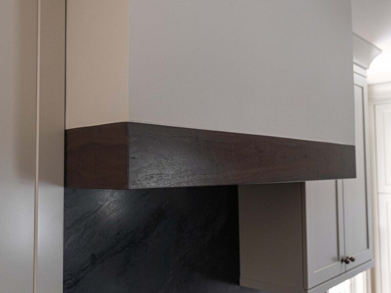 Tulsa kitchen remodel featuring a modern vent hood with wood trim, a gas range top, and a black counter backsplash.