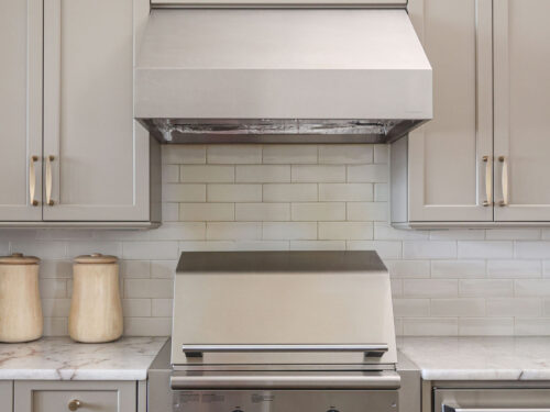 Tulsa kitchen remodeler showcasing a gas grill with a stainless steel vent hood, subway tile backsplash, and coordinating cabinet storage.