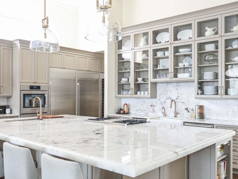 Tulsa kitchen designer and remodeler showcasing a kitchen with a large island with seating, a countertop overhang, and built-in cookbook storage. The high-ceiling space features pendant lights, stainless steel appliances, and wood floors.