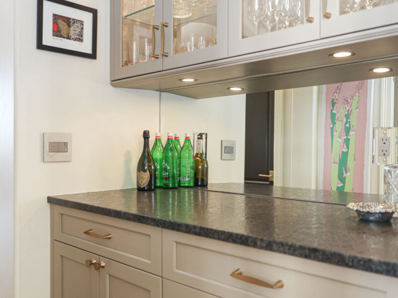 Tulsa kitchen designer and remodeler showcasing a kitchen bar area with a mirror backsplash, glass-front wall cabinets, and base storage, illuminated by puck lighting.
