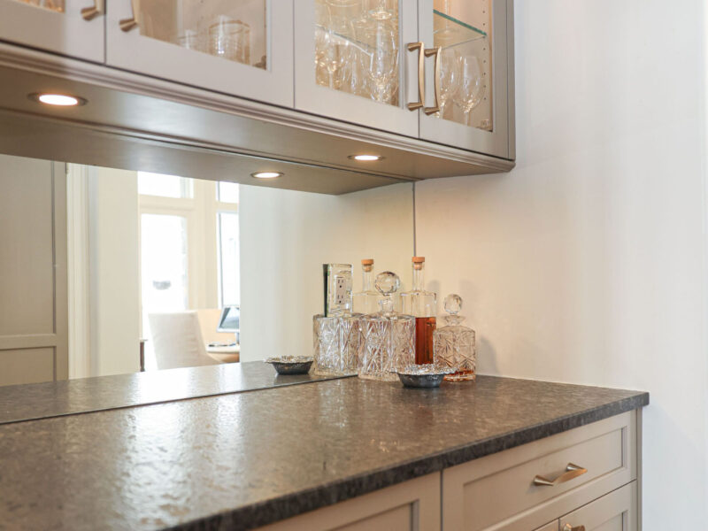 Tulsa kitchen designer and remodeler showcasing a bar area with a mirror backsplash, glass-front wall cabinets, base storage, and puck lighting.