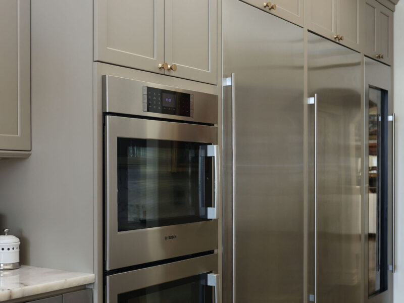 Tulsa kitchen designer and remodeler showcasing a kitchen with built-in double ovens, a full-size side-by-side refrigerator and freezer, and a tall wine refrigerator, surrounded by extensive cabinet storage.