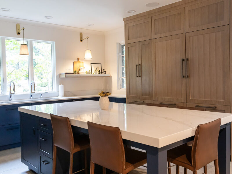 Tulsa kitchen remodel featuring a large island with seating, a Galley Workstation and white counters. The space is illuminated by wall sconces and includes a wood-front refrigerator and freezer.