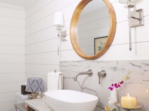 A custom Tulsa bathroom design and remodel featuring a vessel sink vanity, rustic cabinetry, shiplap walls, a round mirror, and elegant sconces.