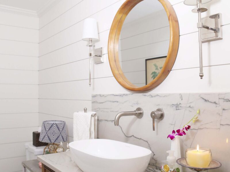A custom Tulsa bathroom design and remodel featuring a vessel sink vanity, rustic cabinetry, shiplap walls, a round mirror, and elegant sconces.