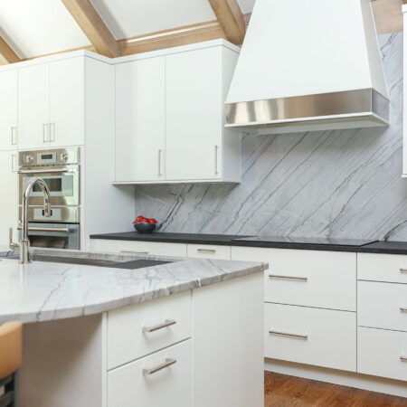 Modern white maple kitchen featuring a cooktop, vent hood, and built-in ovens. Tulsa kitchen designer.