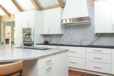 Modern white maple kitchen featuring a cooktop, vent hood, and built-in ovens. Tulsa kitchen designer.