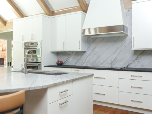 Modern white maple kitchen featuring a cooktop, vent hood, and built-in ovens. Tulsa kitchen designer.