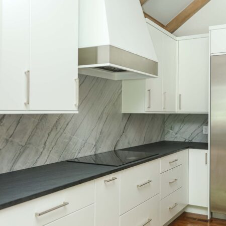 Modern white kitchen featuring an induction cooktop, integrated vent hood, and a seamless countertop backsplash. Tulsa kitchen remodeler.