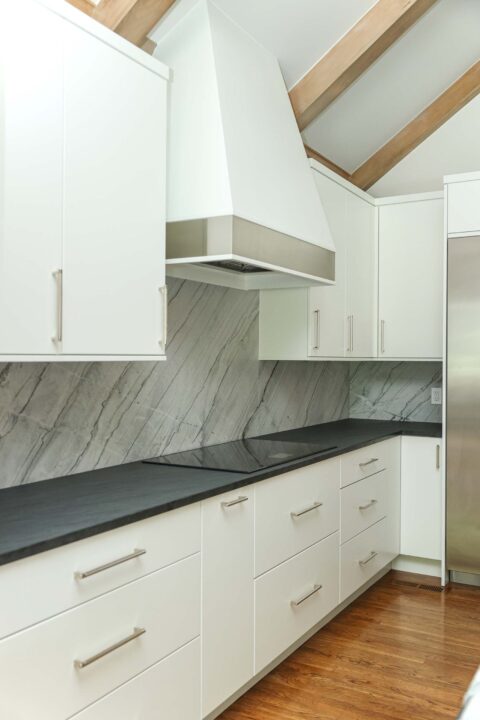 Modern white kitchen featuring an induction cooktop, integrated vent hood, and a seamless countertop backsplash. Tulsa kitchen remodeler.
