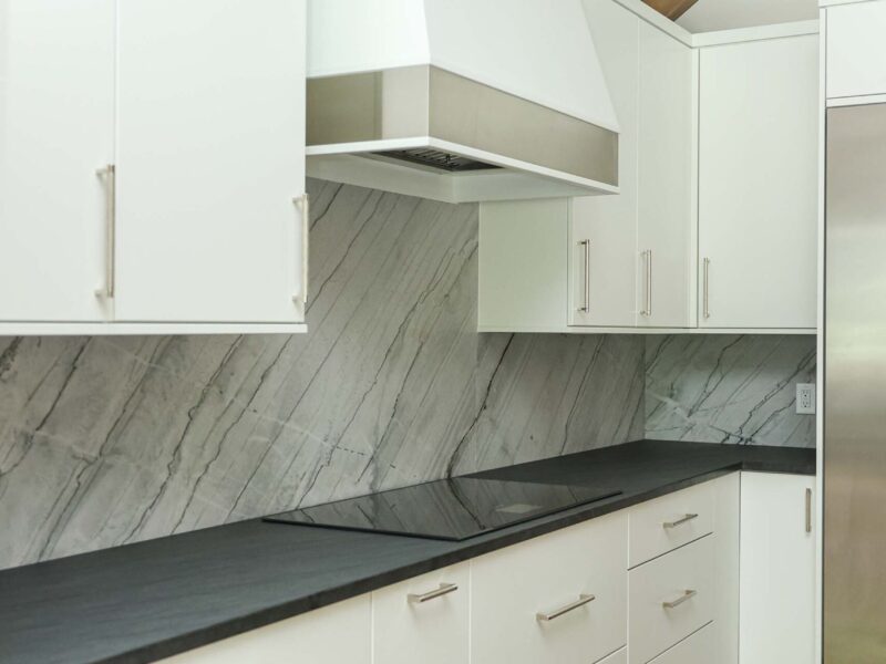 Modern white kitchen featuring an induction cooktop, integrated vent hood, and a seamless countertop backsplash. Tulsa kitchen remodeler.