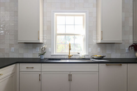 Greige kitchen with a workstation sink and black counters. The design features a tile backsplash. Tulsa kitchen design and remodel.