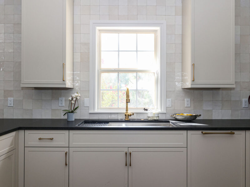 Greige kitchen with a workstation sink and black counters. The design features a tile backsplash. Tulsa kitchen design and remodel.
