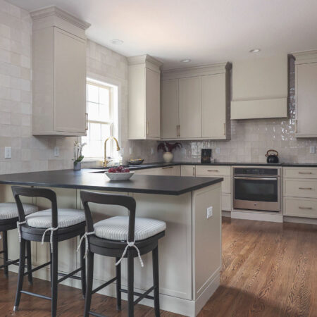 Greige kitchen remodel featuring a large peninsula with seating, black countertops, GE appliances, and a tile backsplash.