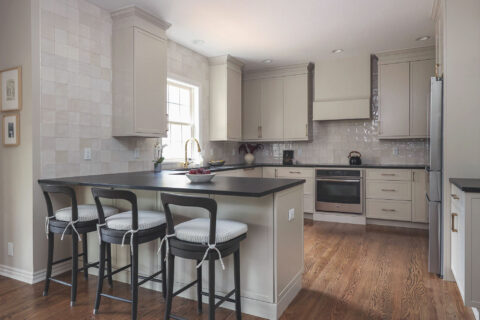 Greige kitchen remodel featuring a large peninsula with seating, black countertops, GE appliances, and a tile backsplash.