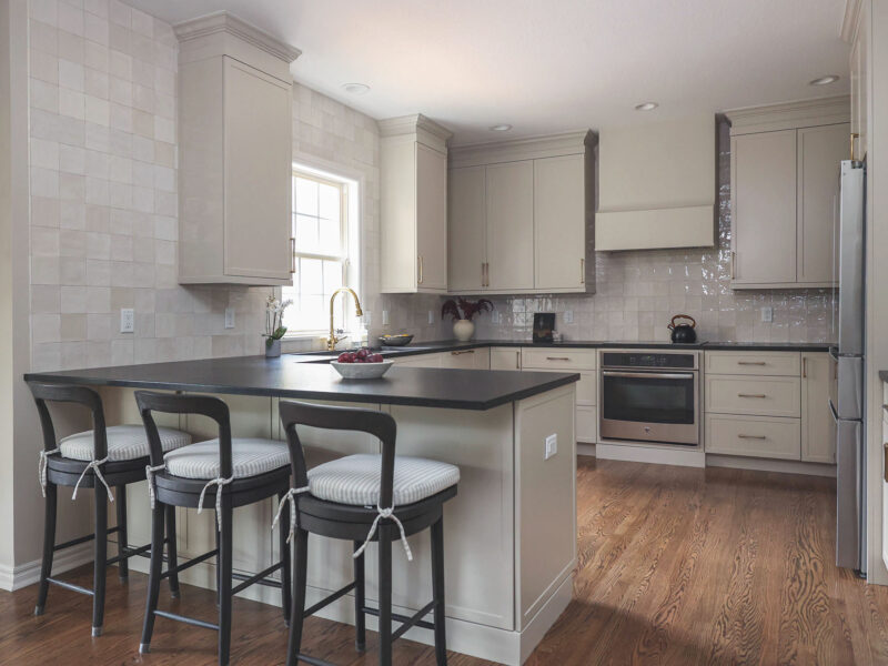 Greige kitchen remodel featuring a large peninsula with seating, black countertops, GE appliances, and a tile backsplash.
