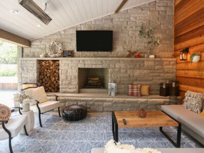 Spacious open-concept patio featuring comfortable lounge seating area and natural stone fireplace with firewood storage in Tulsa design and remodel.
