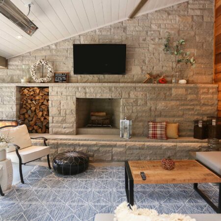 Spacious open-concept patio featuring comfortable lounge seating area and natural stone fireplace with firewood storage in Tulsa design and remodel.