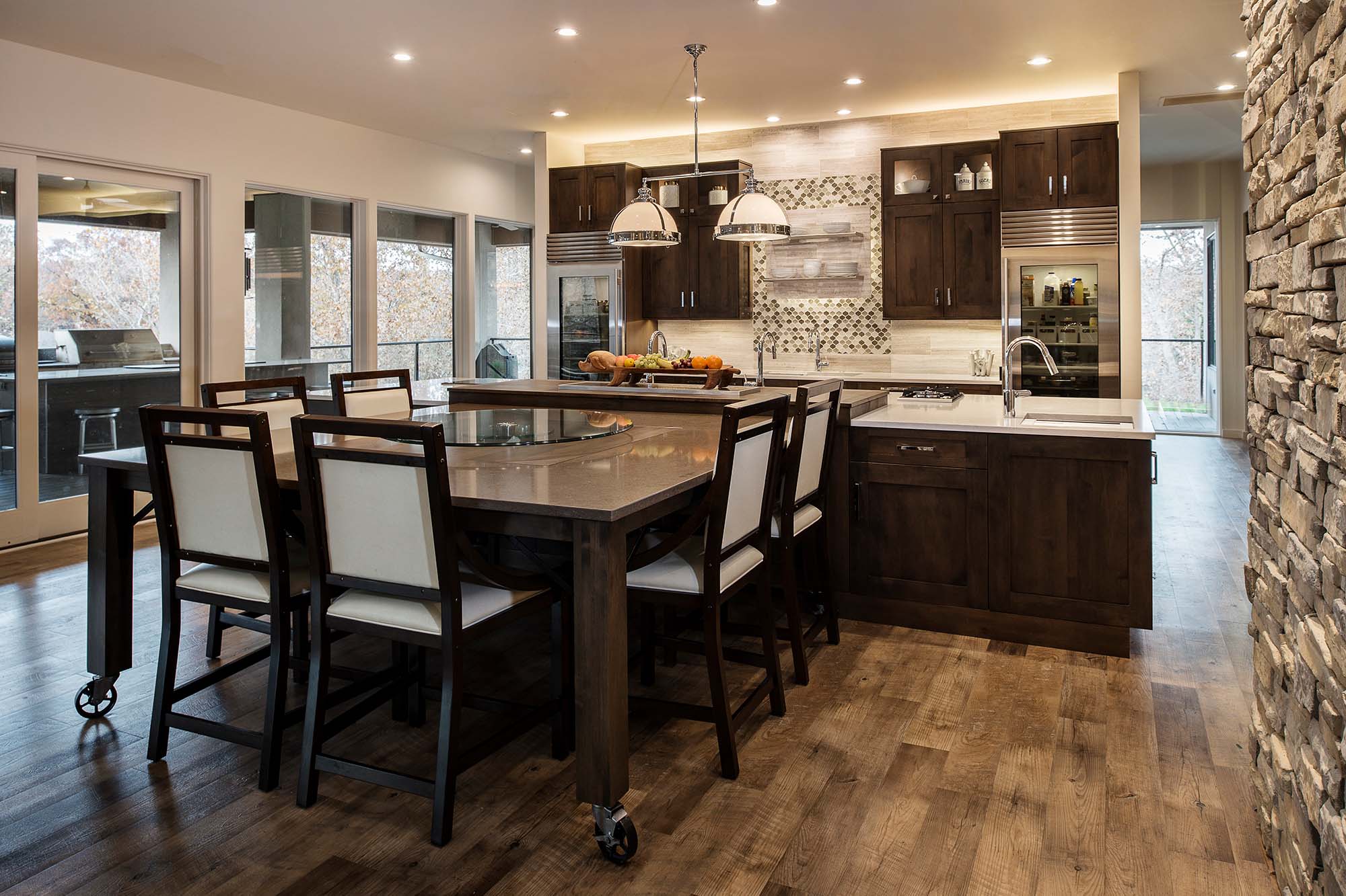 South Tulsa kitchen featuring movable table, pop-up television, large island with Caesarstone countertops, Sub-Zero Wolf appliances, cabinet storage, and floating shelves in kitchen remodel.